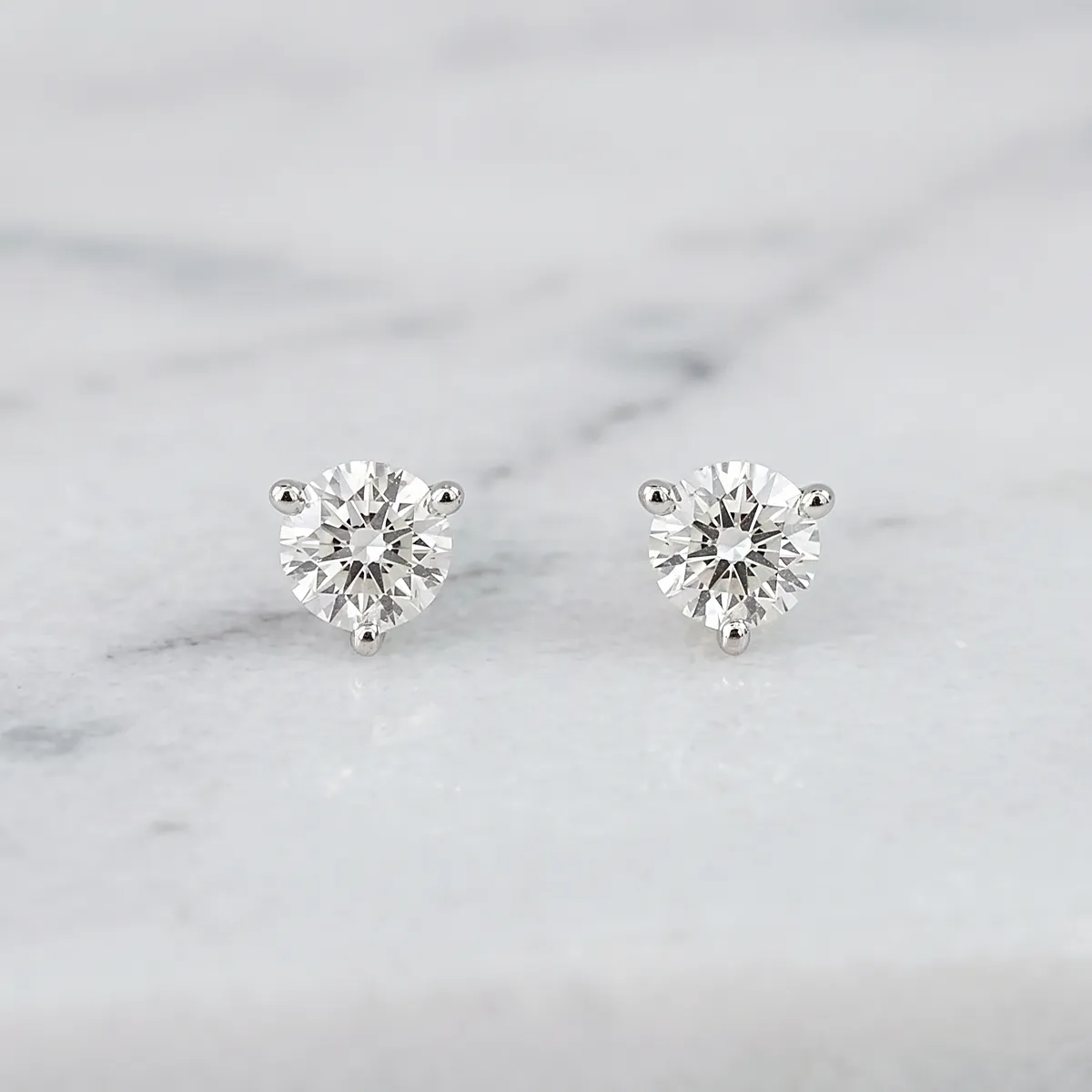 Diamond stud earrings on a marble surface.