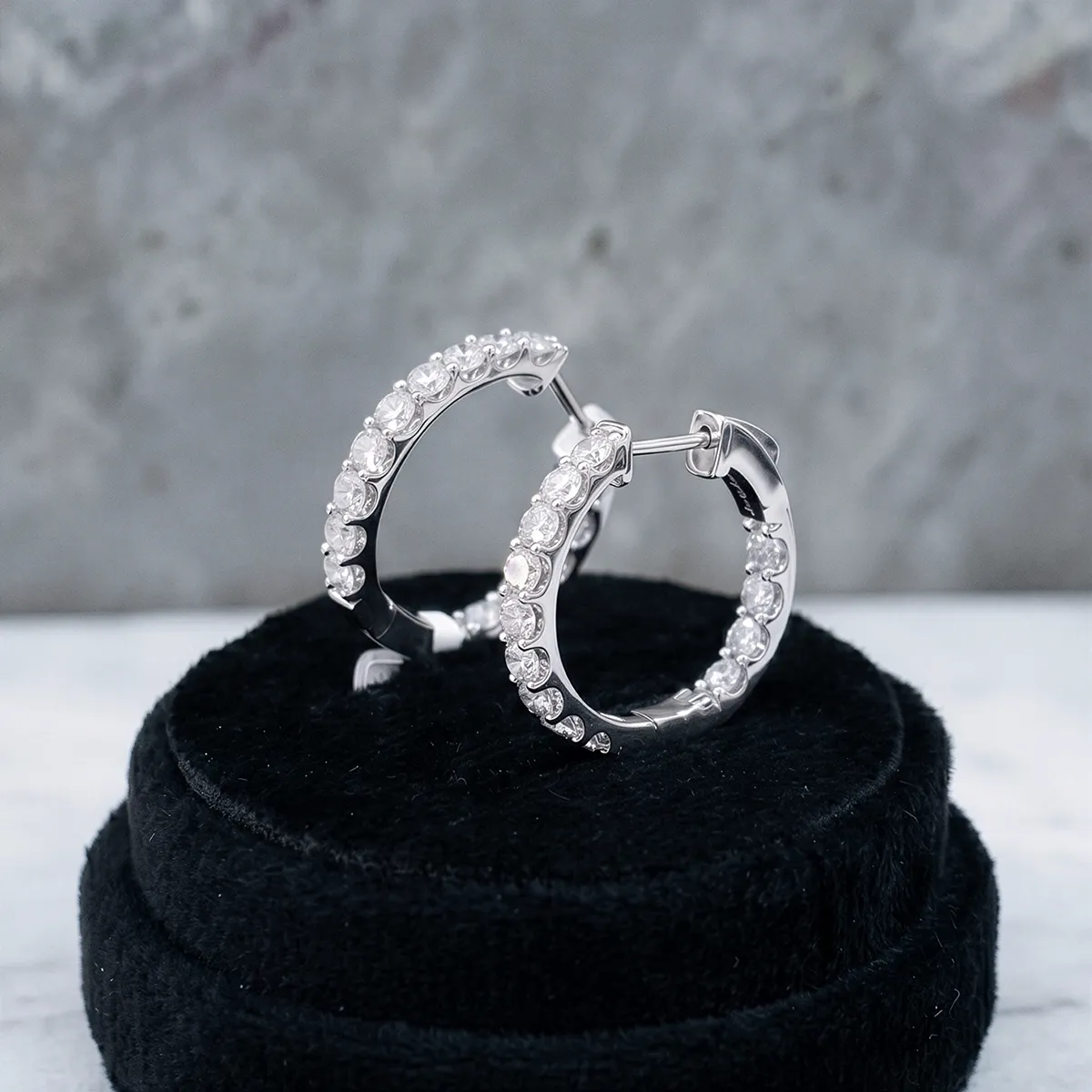 Diamond hoop earrings with stones on black velvet display.