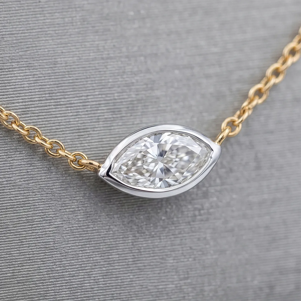 A marquise-cut diamond pendant on a gold chain displayed on a textured gray background.