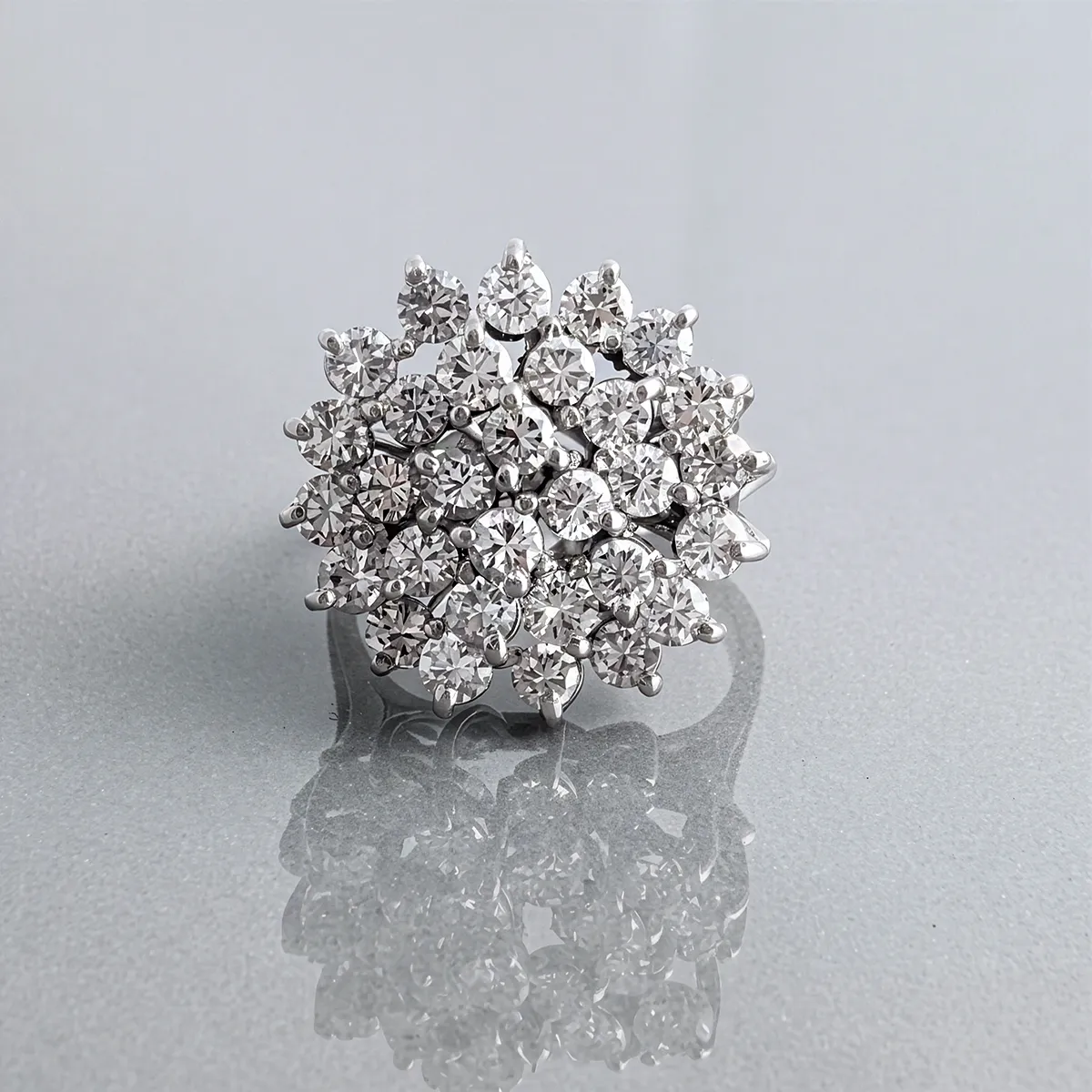 A sparkling diamond cluster ring on a reflective surface.