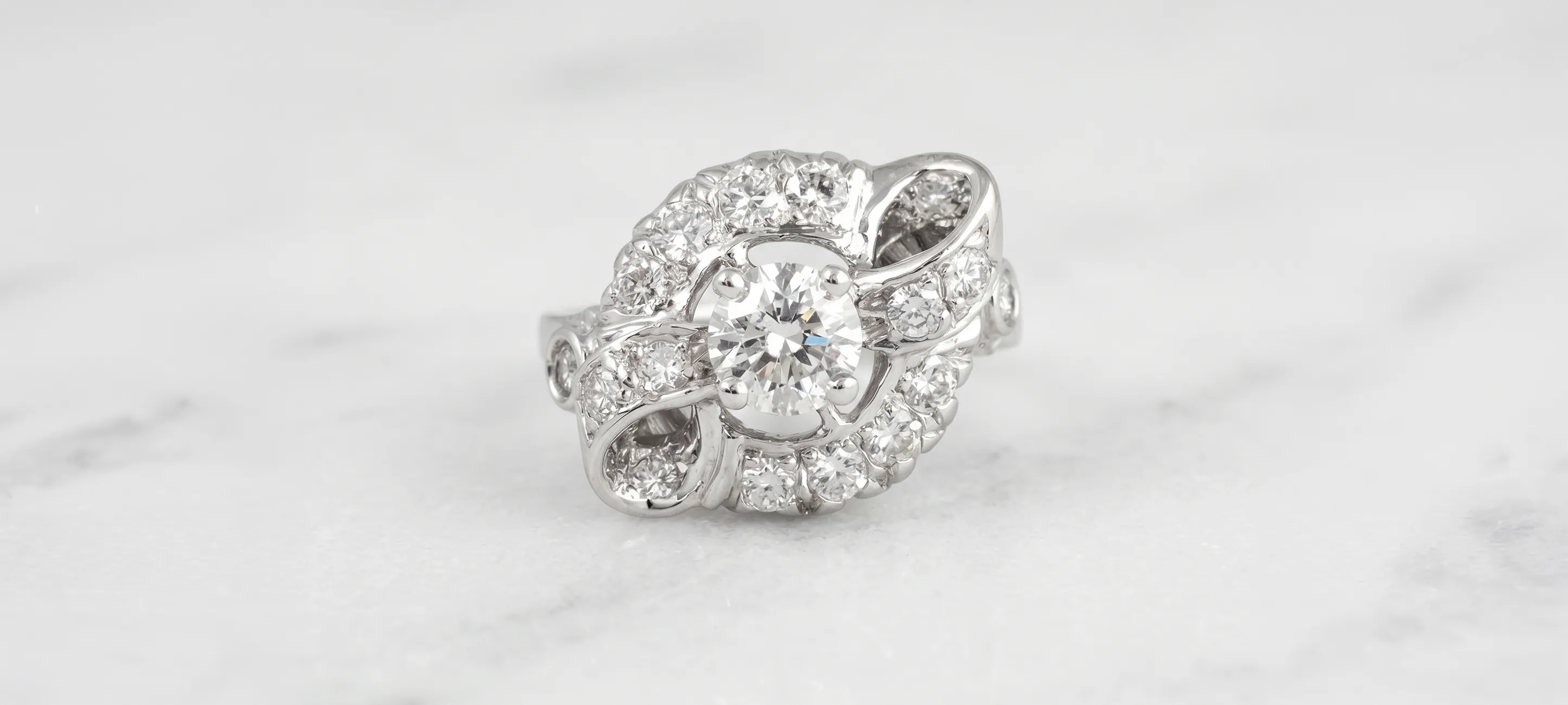 Elegant diamond ring with intricate design on a marble surface.