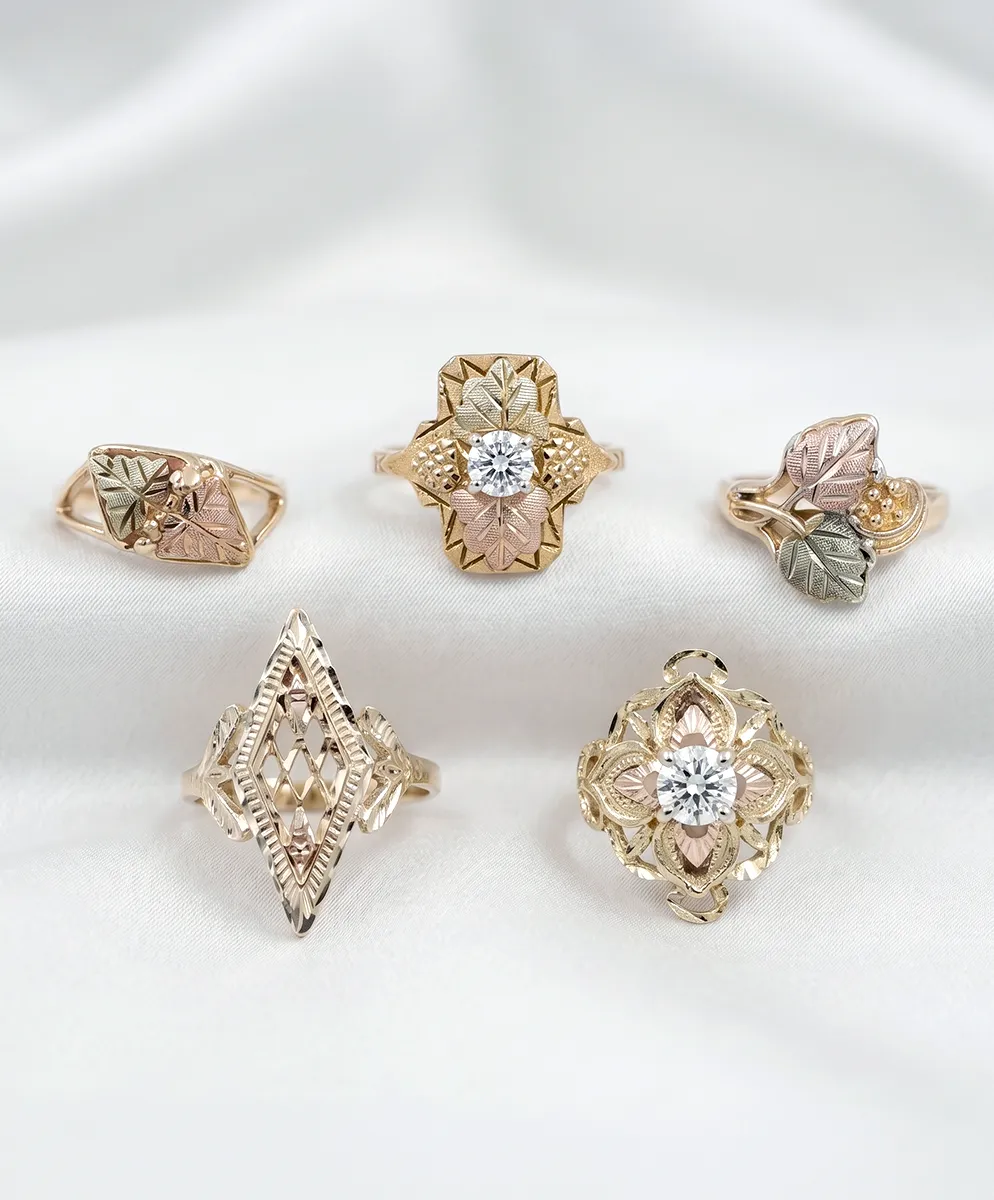 Five intricately designed gold rings with leaf motifs and diamonds on a white fabric background.