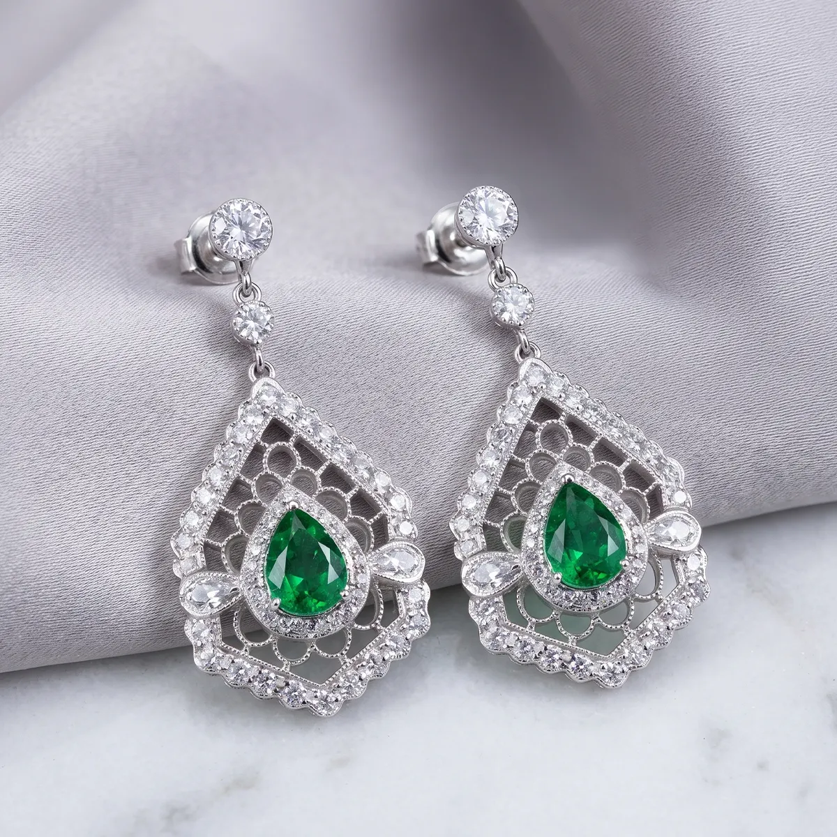 Estate earrings with green gemstones and diamonds on a gray fabric background. Explore estate earrings.