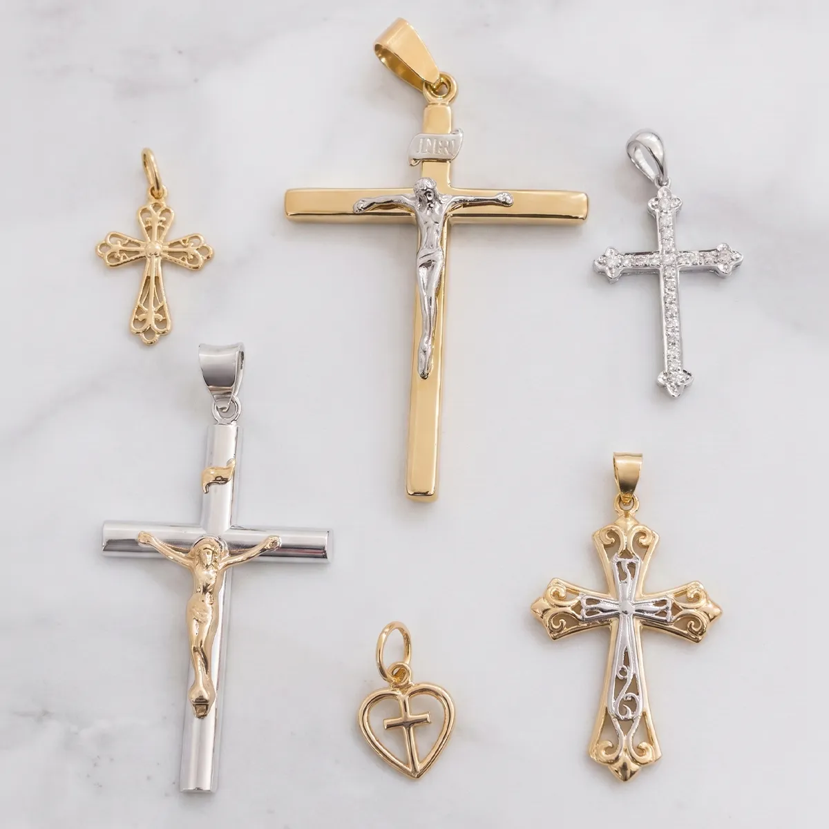 Religious cross pendants in gold and silver displayed on a marble surface. Explore more at Georgetown Jewelers.