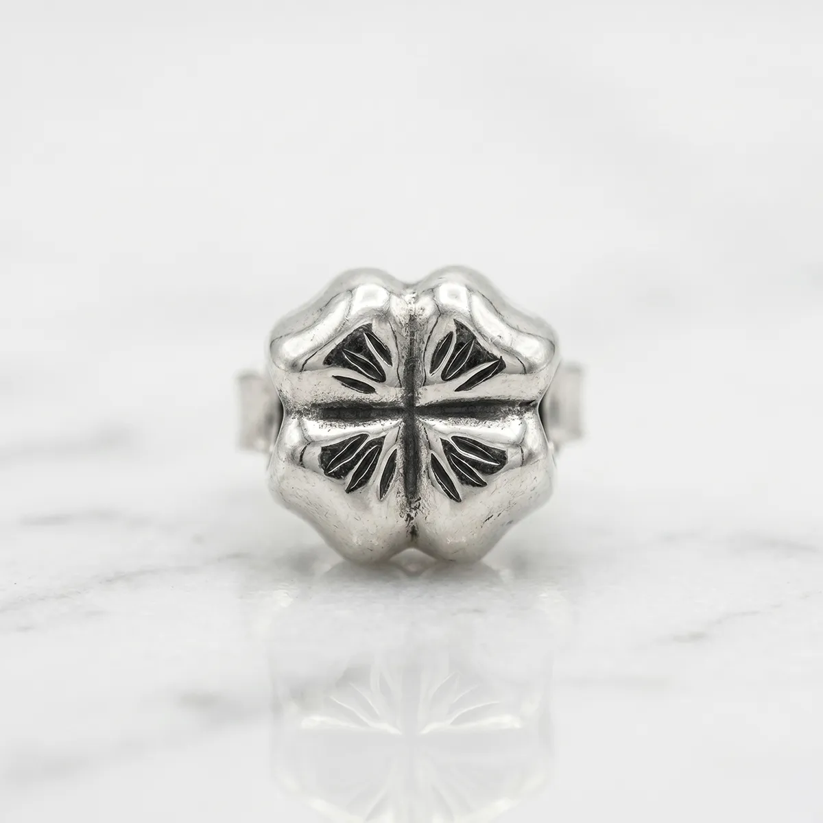 Silver clover-shaped charm with engraved details on a marble surface.
