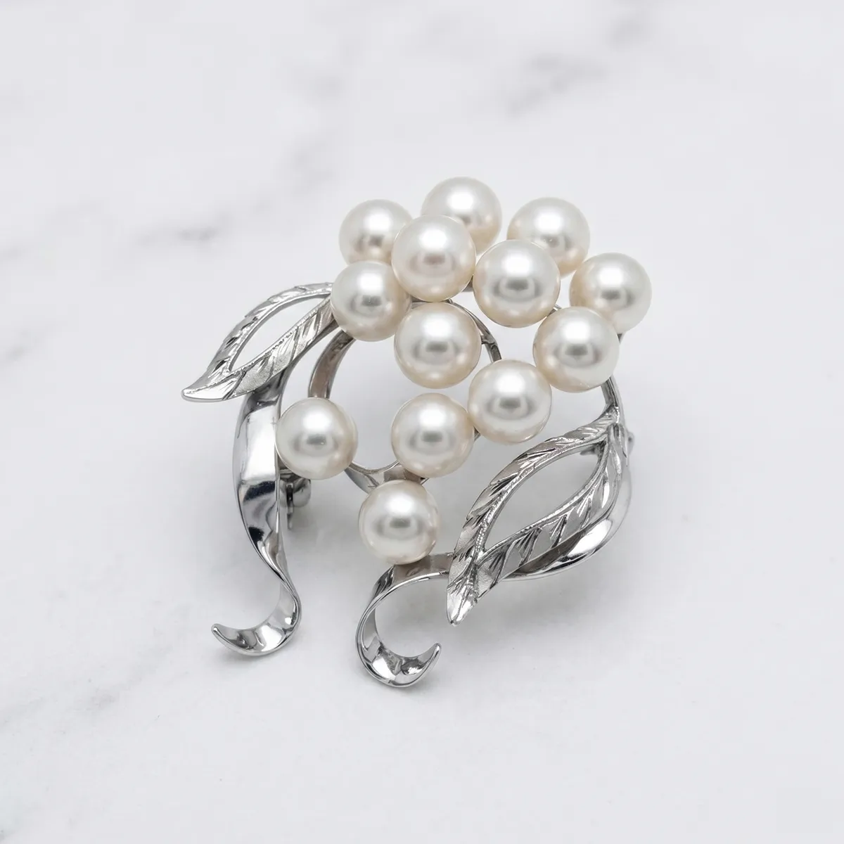 Silver brooch with pearls and leaf design on a marble surface.