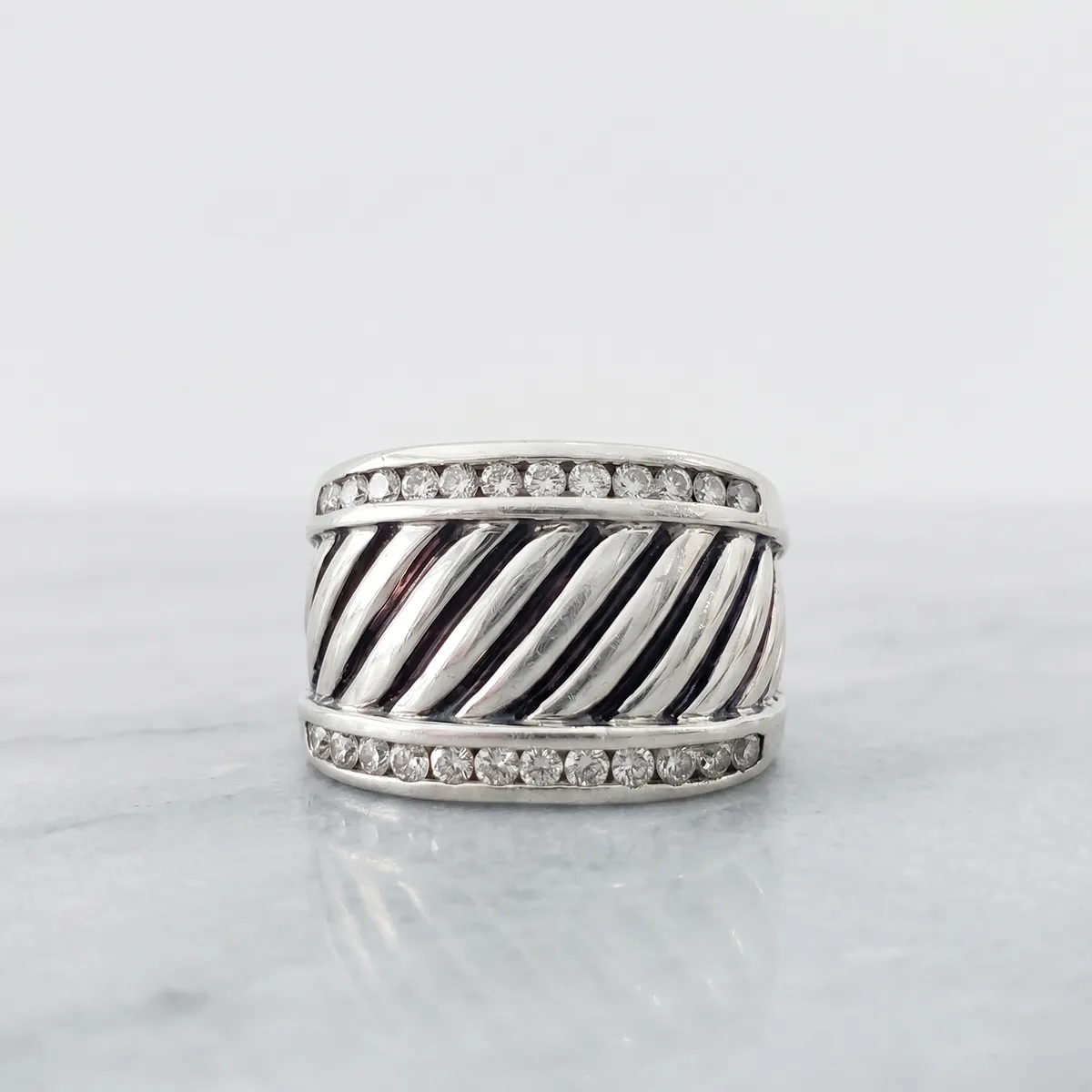 Silver ring with diagonal grooves and diamond accents on marble surface.