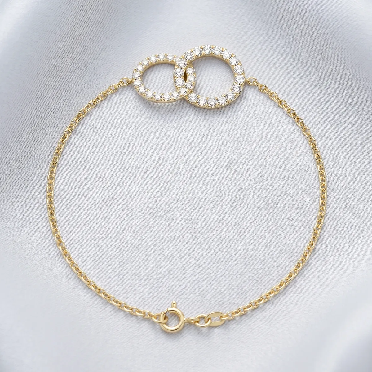 Gold bracelet with interlocking diamond circles on a soft fabric background. Shop bracelets at Georgetown Jewelers.