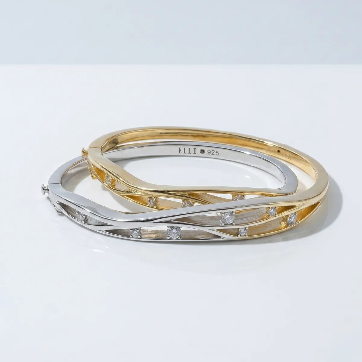 Two intertwined gold and silver cuff bracelets with diamond accents.