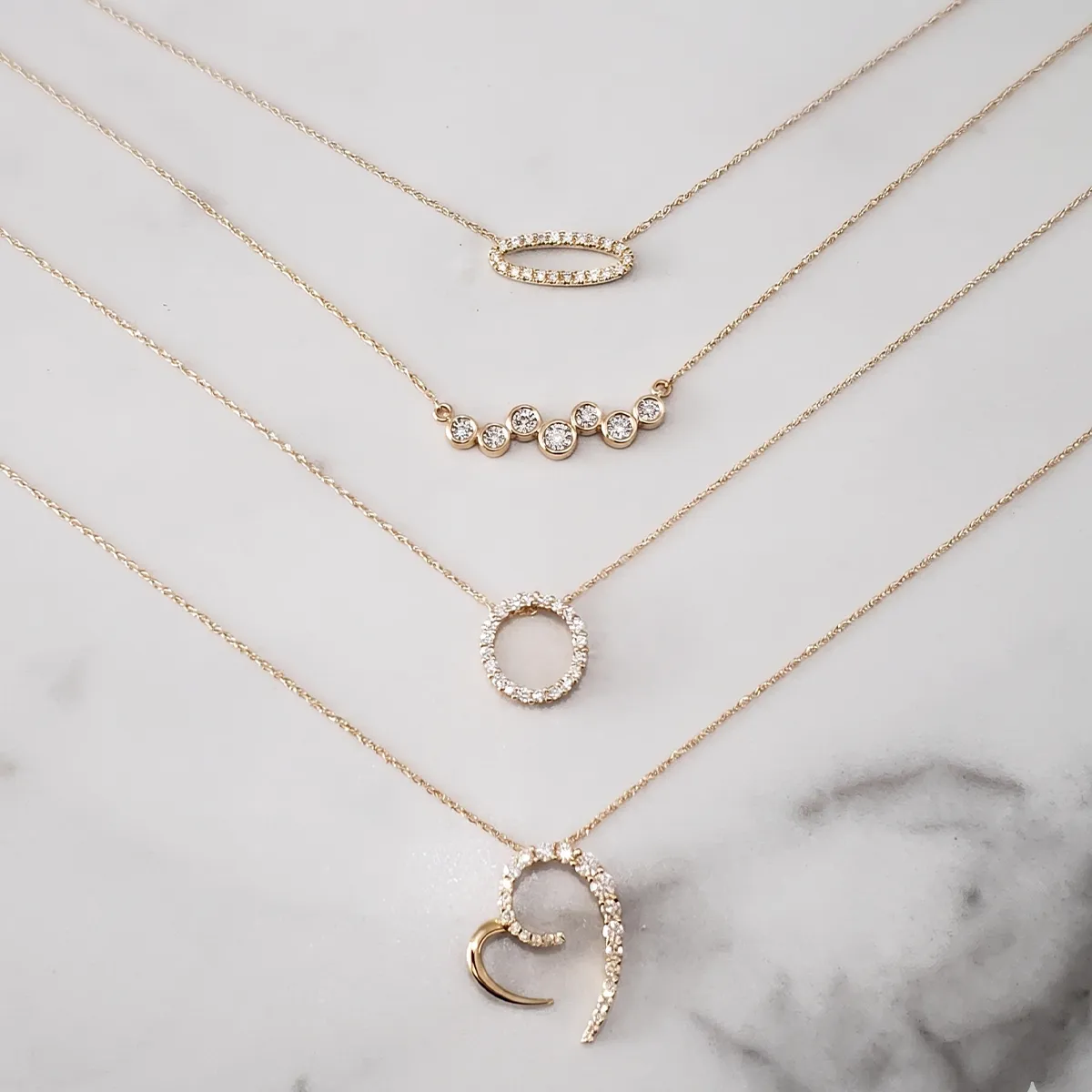 Layered gold necklaces with various pendants on a marble surface. Shop necklaces at Georgetown Jewelers.
