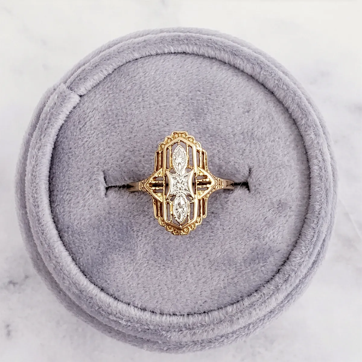 Elegant gold ring with intricate design and diamonds on a gray cushion. Shop rings at Georgetown Jewelers.