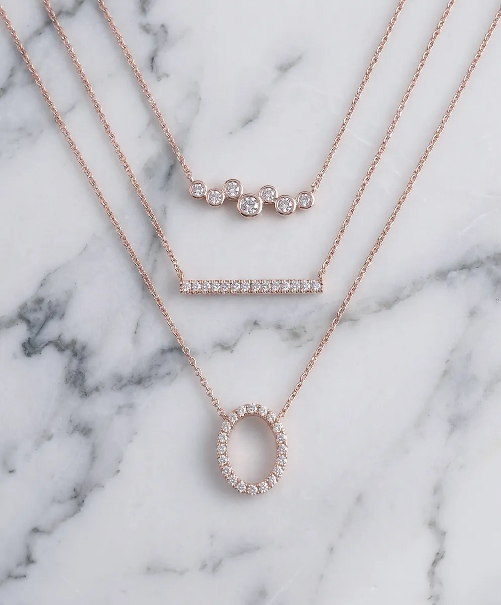 Layered rose gold necklaces with diamond accents on a marble surface.