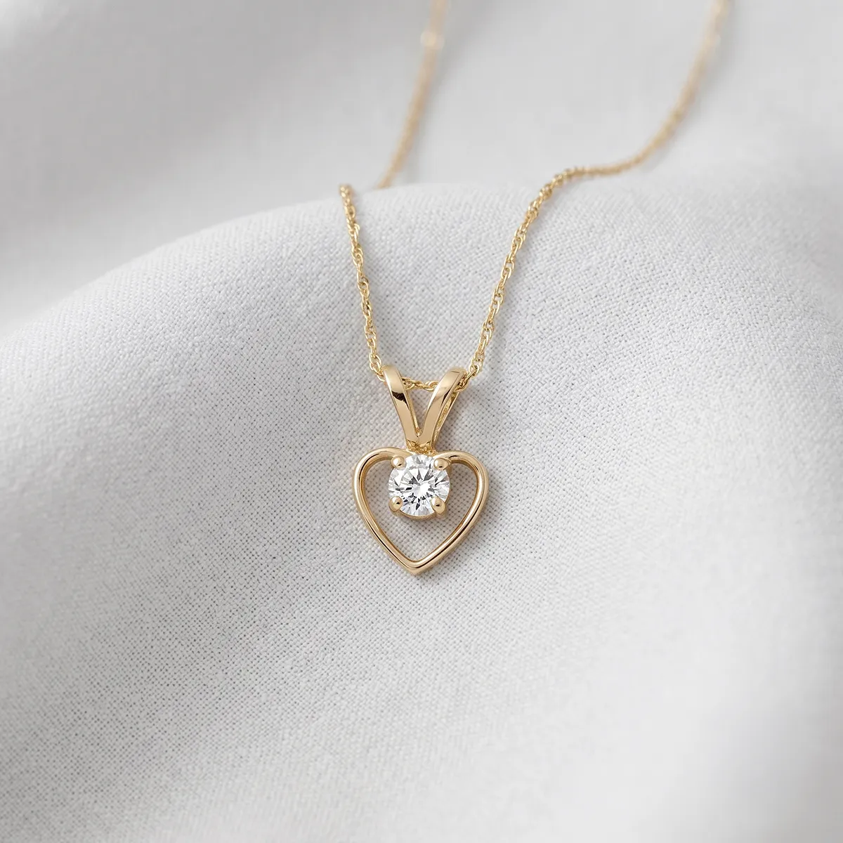 Gold heart pendant necklace with a diamond on a white fabric background.
