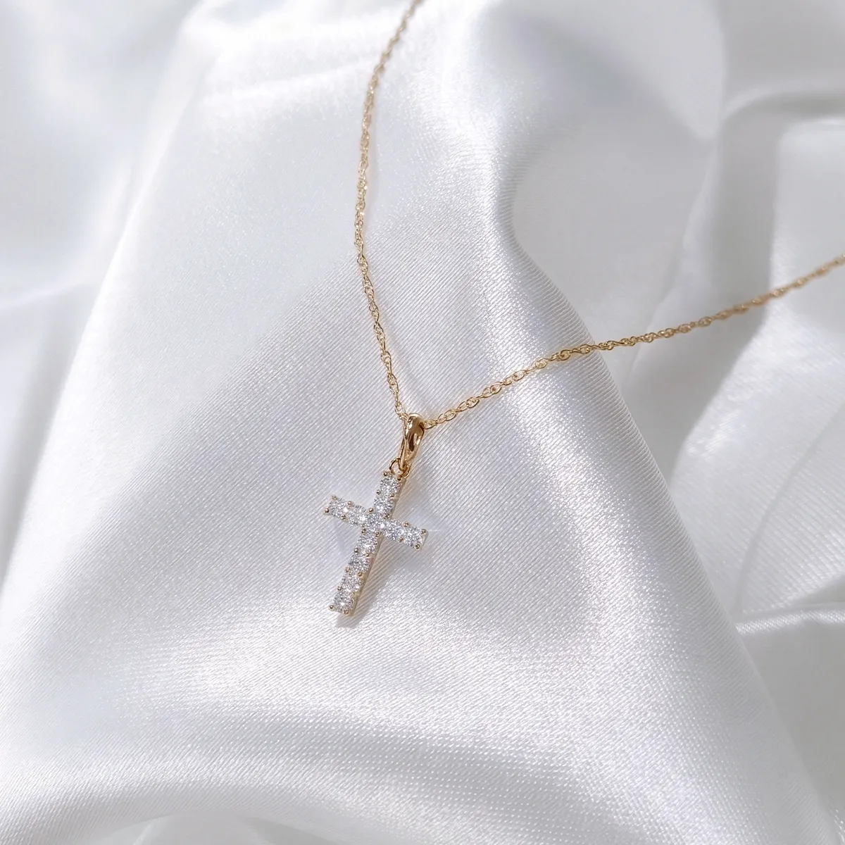 Gold chain with diamond cross pendant on white satin. Explore religious jewelry at Georgetown Jewelers.