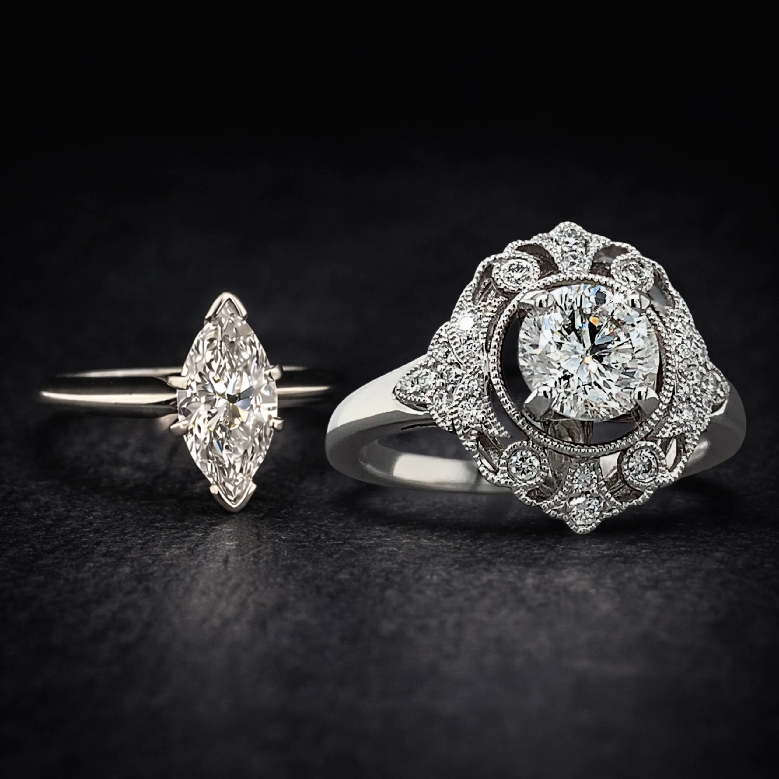 A marquise-cut diamond ring and a vintage style engagement ring on a dark surface.