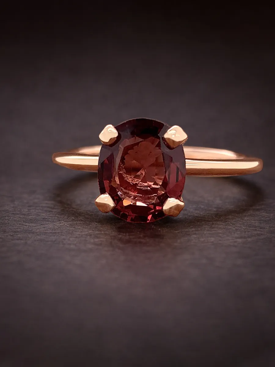 A rose gold ring with an oval red gemstone on a dark background.