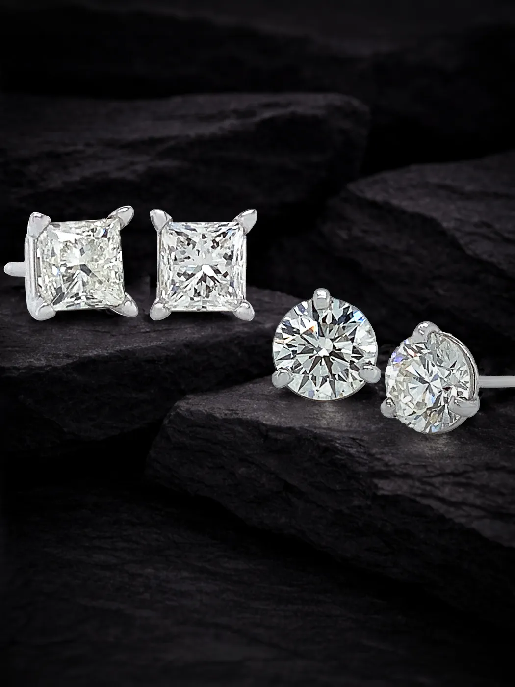 Diamond stud earrings, square and round cut, displayed on dark stones.