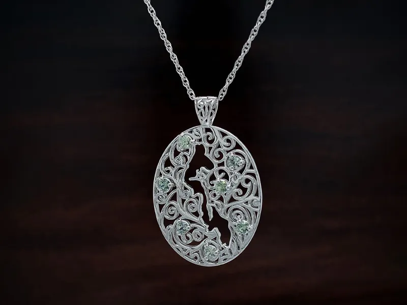 Ornate silver pendant with intricate swirls and green gemstones on a chain, set against a dark background.