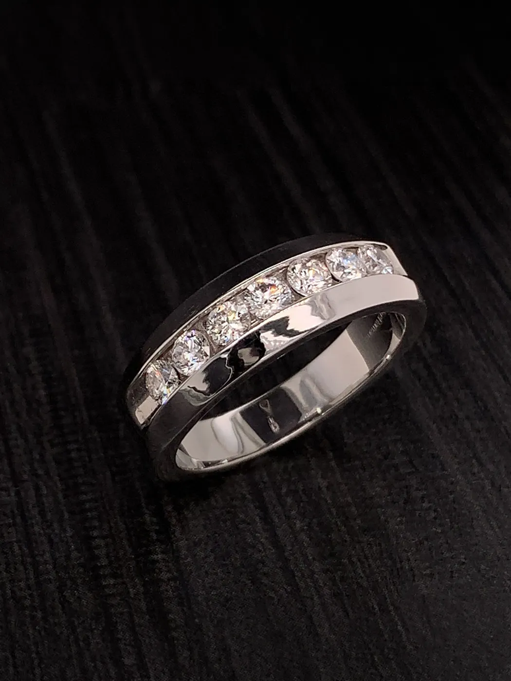 Elegant silver wedding band with embedded diamonds on dark background.