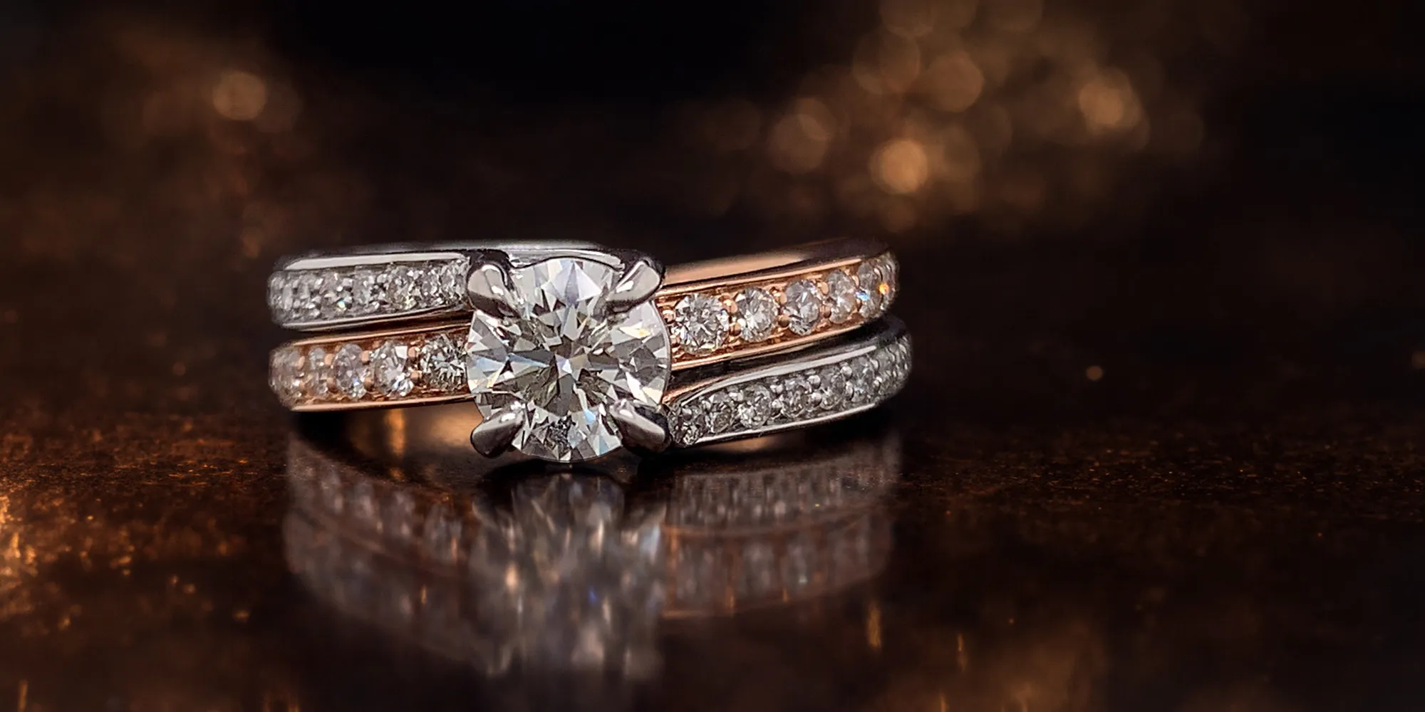 Diamond engagement ring with two bands on a dark reflective surface.