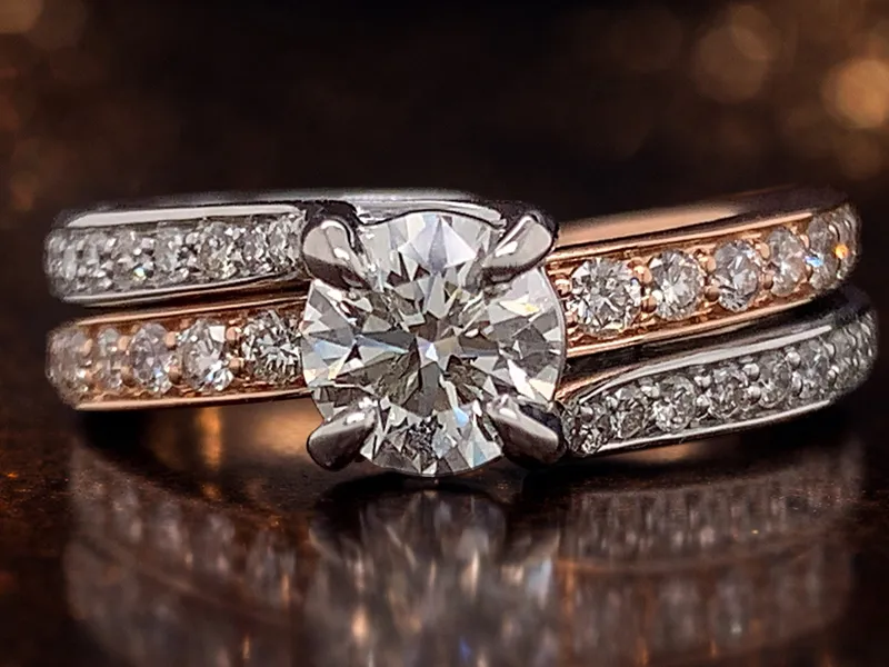 Diamond engagement ring with two bands on a dark reflective surface.