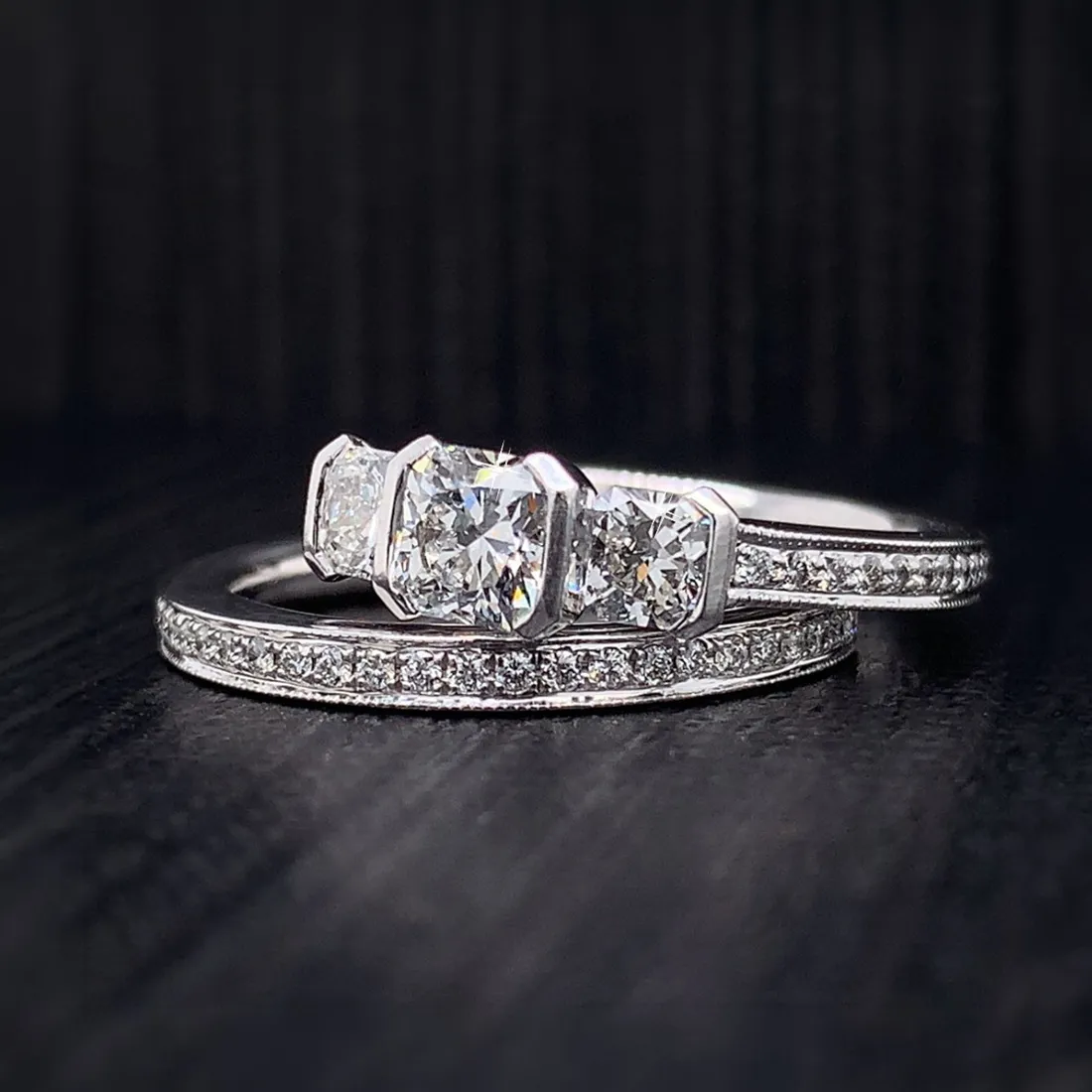 Elegant diamond engagement and wedding ring set on dark background.
