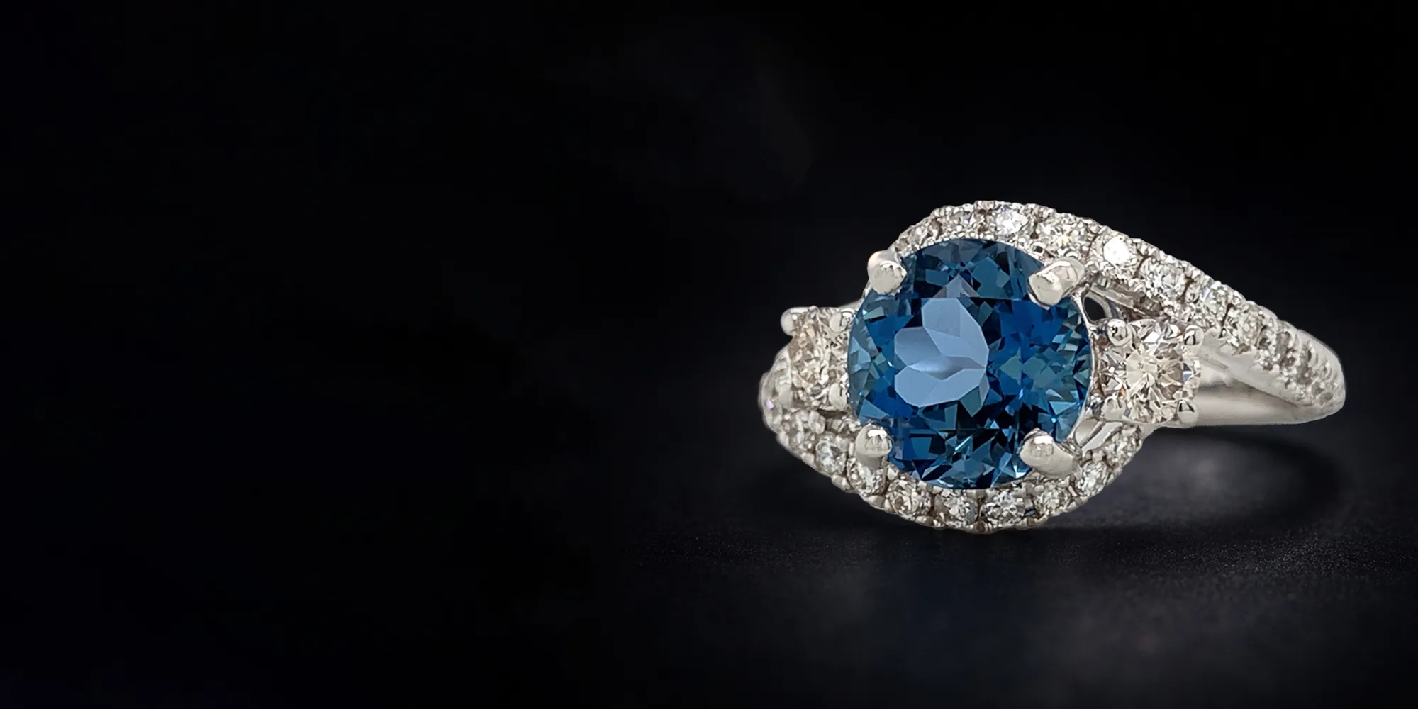 Elegant ring with a blue gemstone and diamond accents on a dark background.
