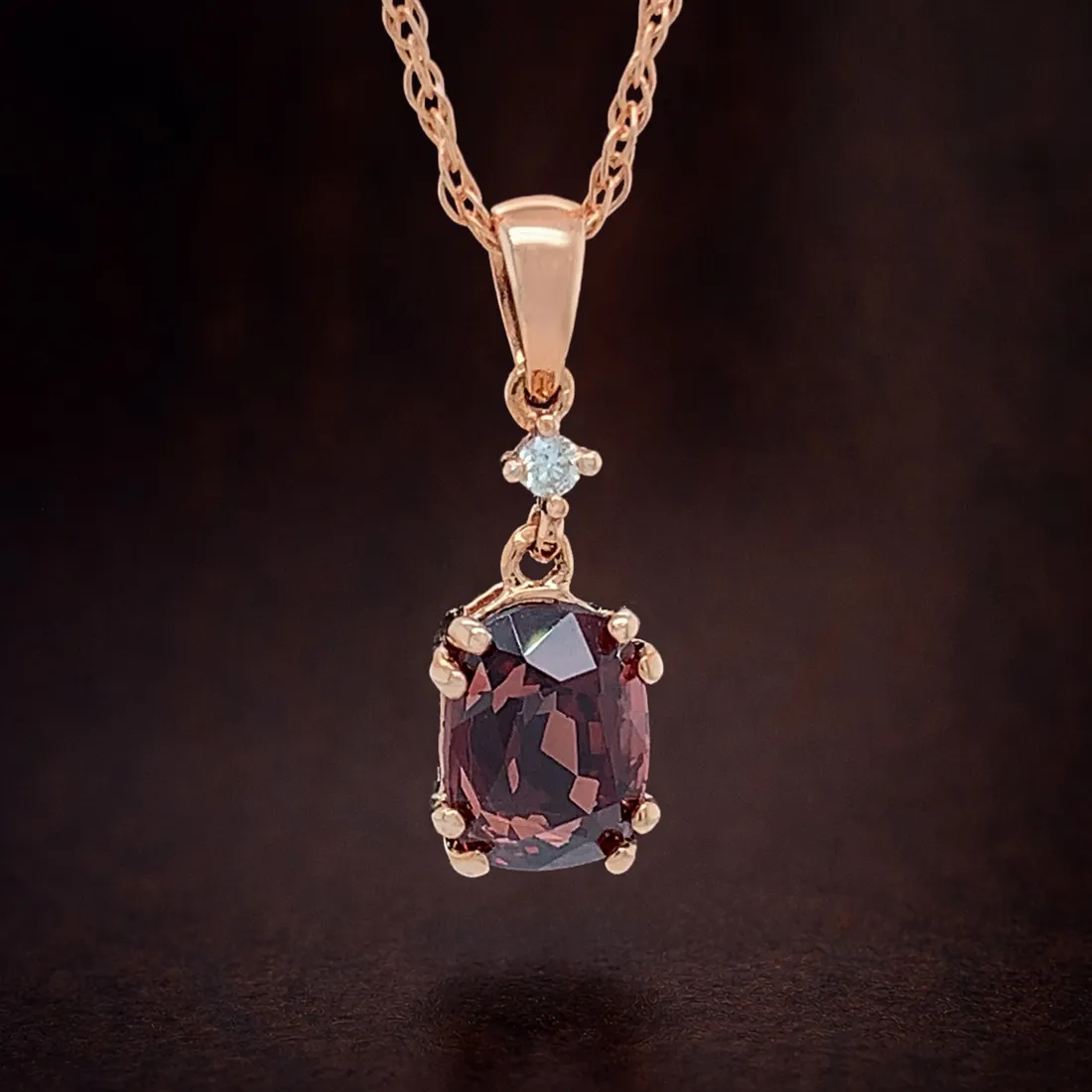 Rose gold necklace with a dark gemstone pendant and small diamond on a dark background.