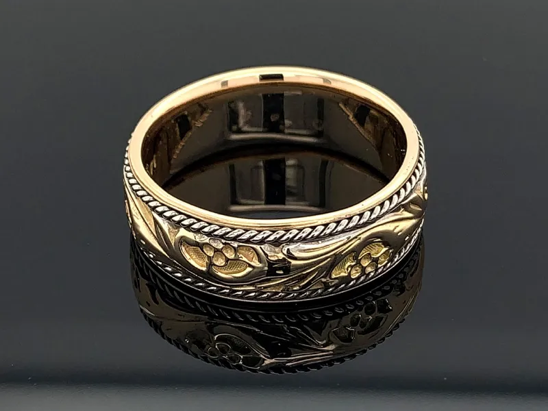 Gold ring with intricate floral engravings on a reflective black surface.