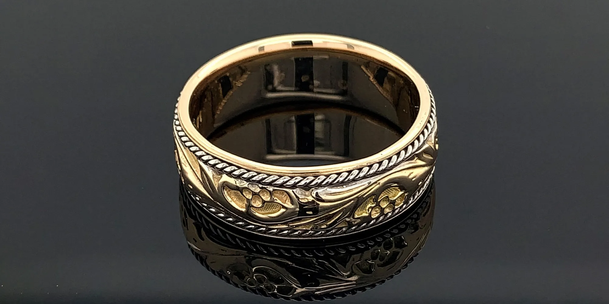 Gold ring with intricate floral engravings on a reflective black surface.