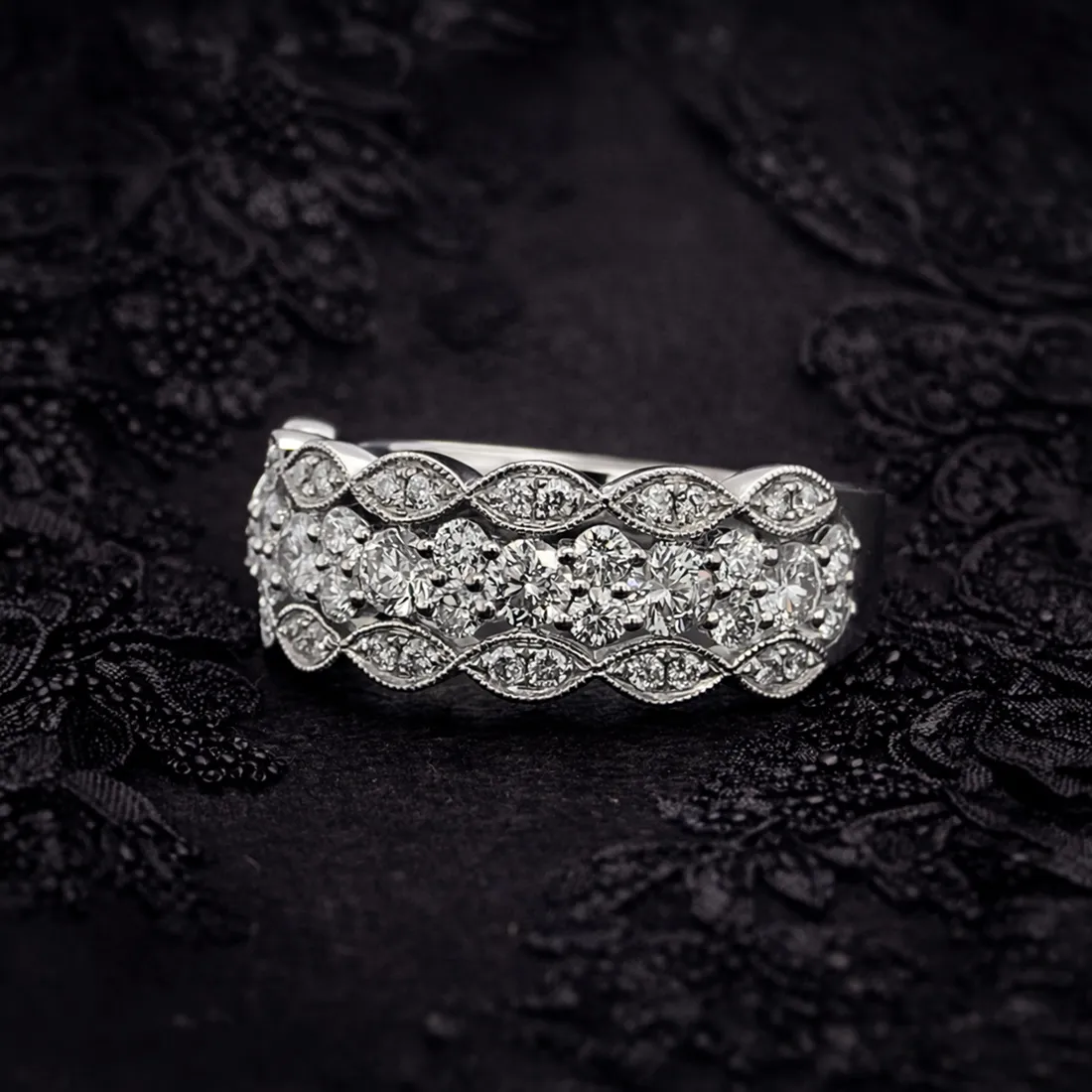 Elegant diamond ring with intricate design on black lace background.