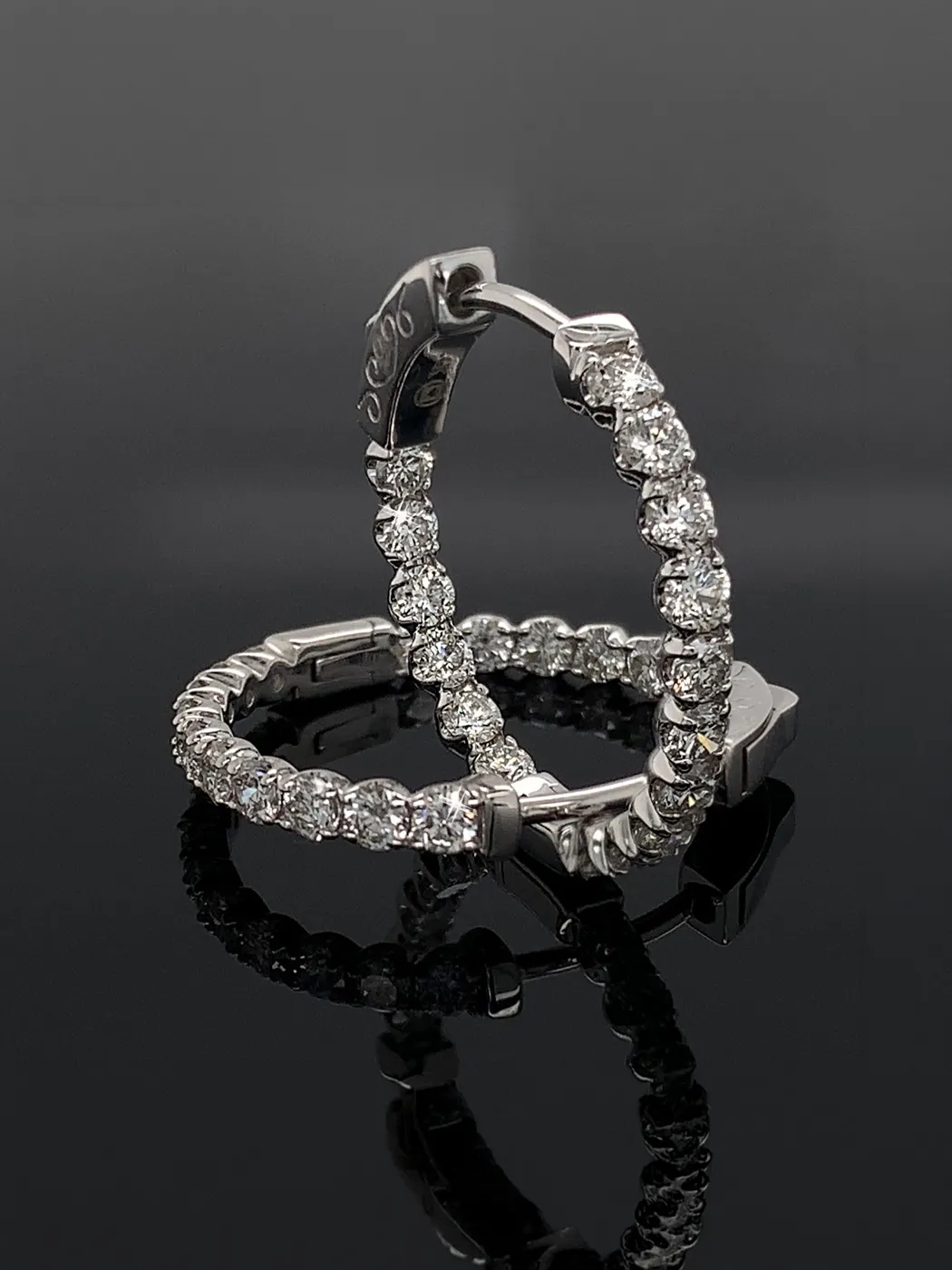 Diamond hoop earrings with sparkling stones on a reflective black surface.