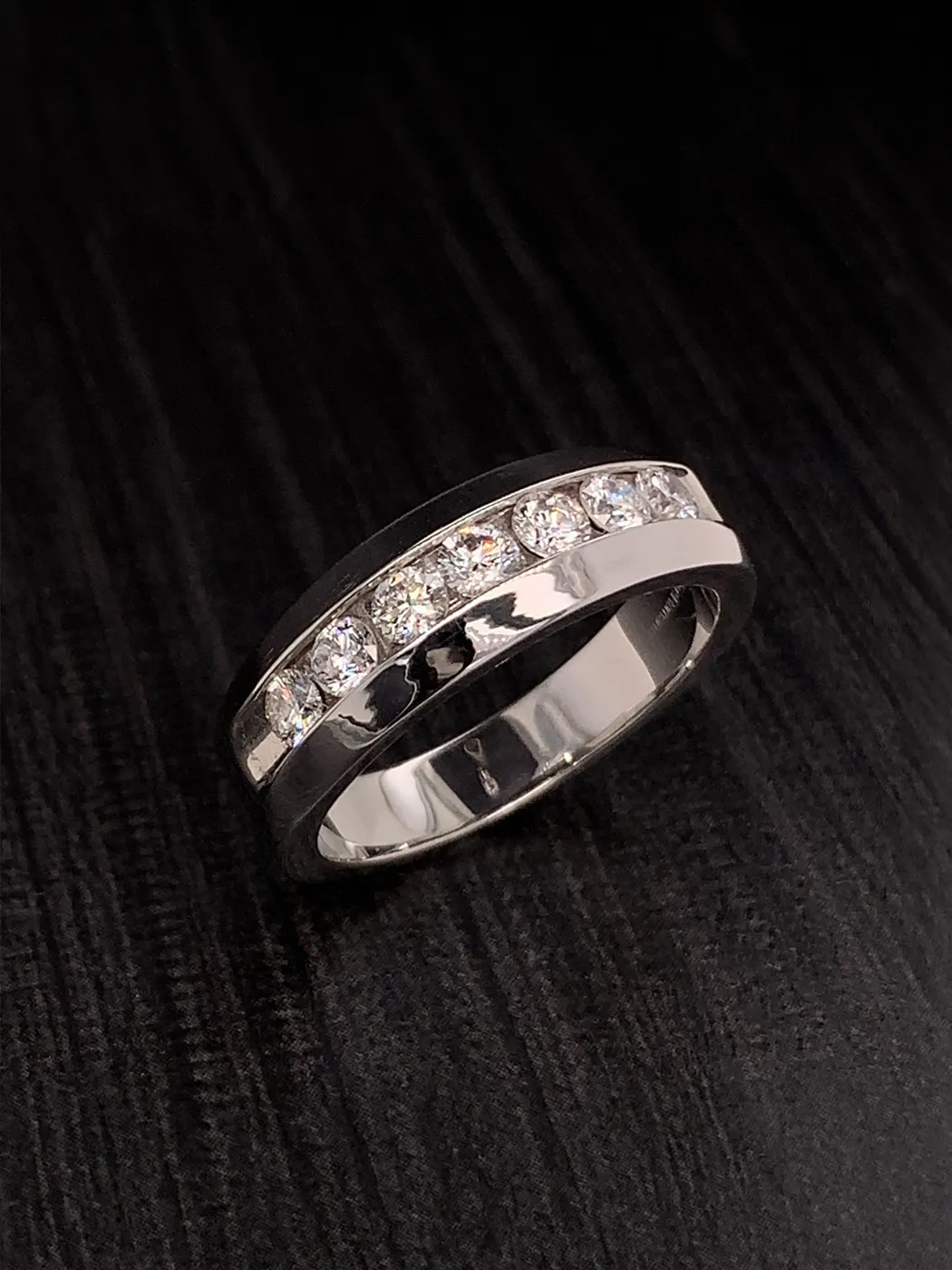 Diamond-studded silver wedding band on dark wood surface.