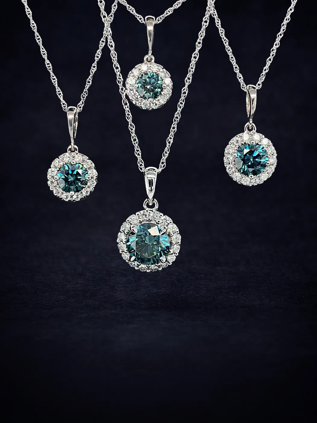 Four diamond necklaces with blue gemstones on silver chains against a dark background.
