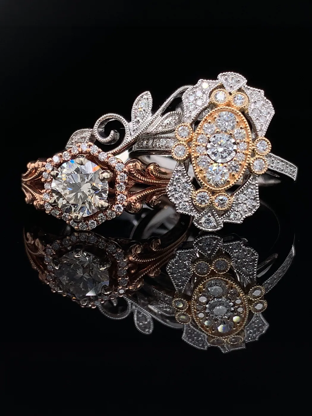 Two ornate diamond rings with intricate designs on a black reflective surface.