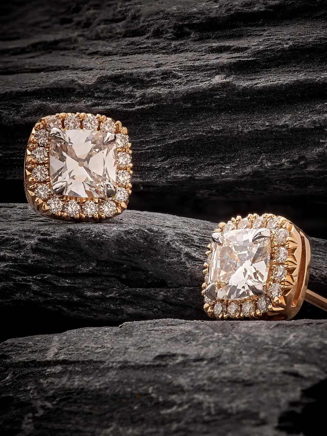 Diamond stud earrings with halo setting on dark textured background.