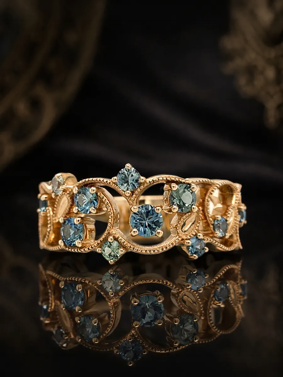 Ornate gold ring with blue gemstones on a reflective surface.