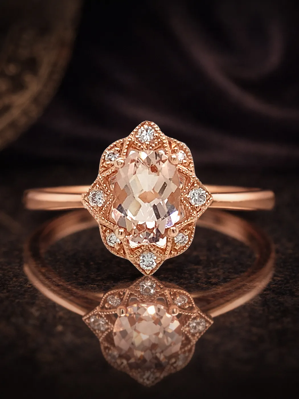 Rose gold ring with a morganite center stone and diamond accents on a dark reflective surface.
