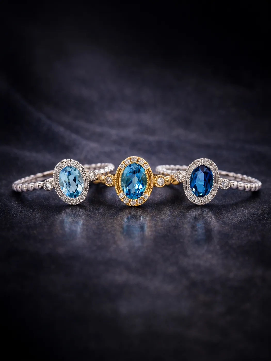 Three gemstone rings with blue stones on a dark surface.