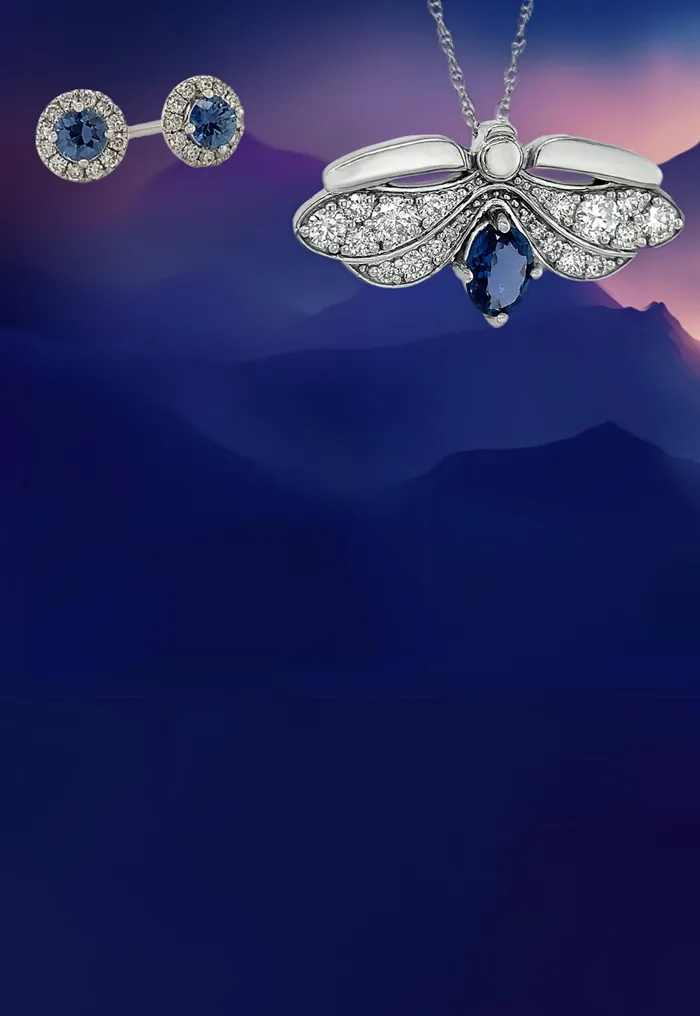 Jewelry pieces with blue sapphires on a mountain-themed background. Click to shop Yogo Sapphire Jewelry.
