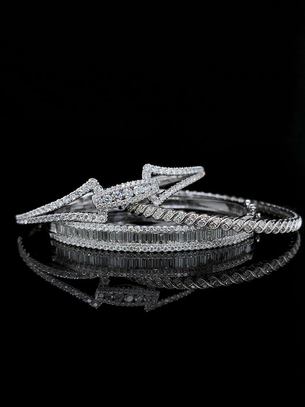 Diamond bracelets with intricate designs on a reflective black surface.