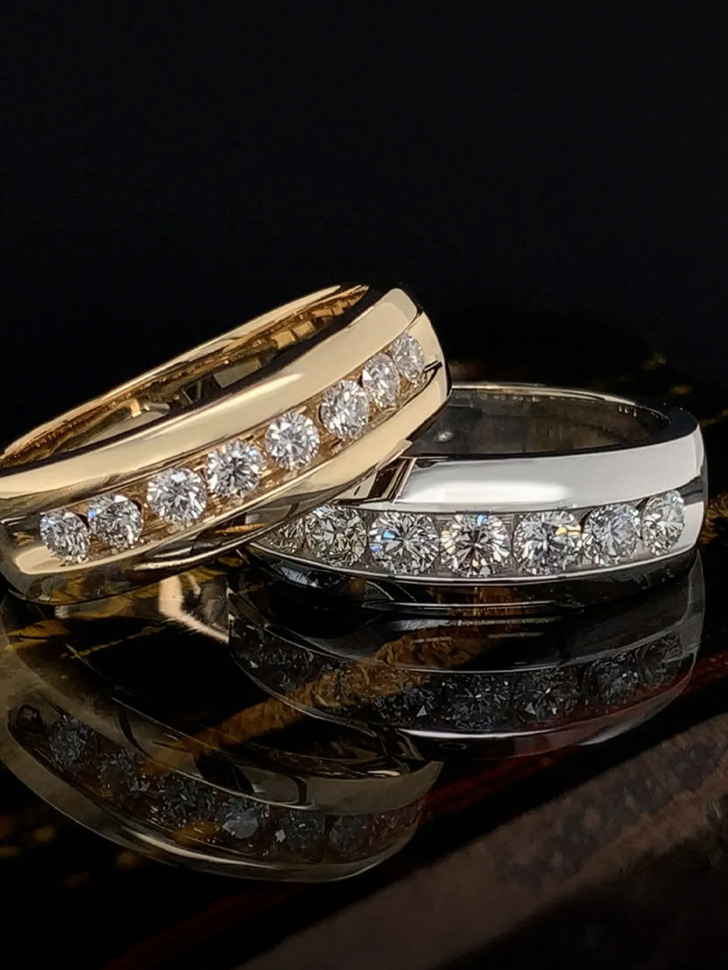 Two gold and silver diamond-studded men's rings on a reflective surface.