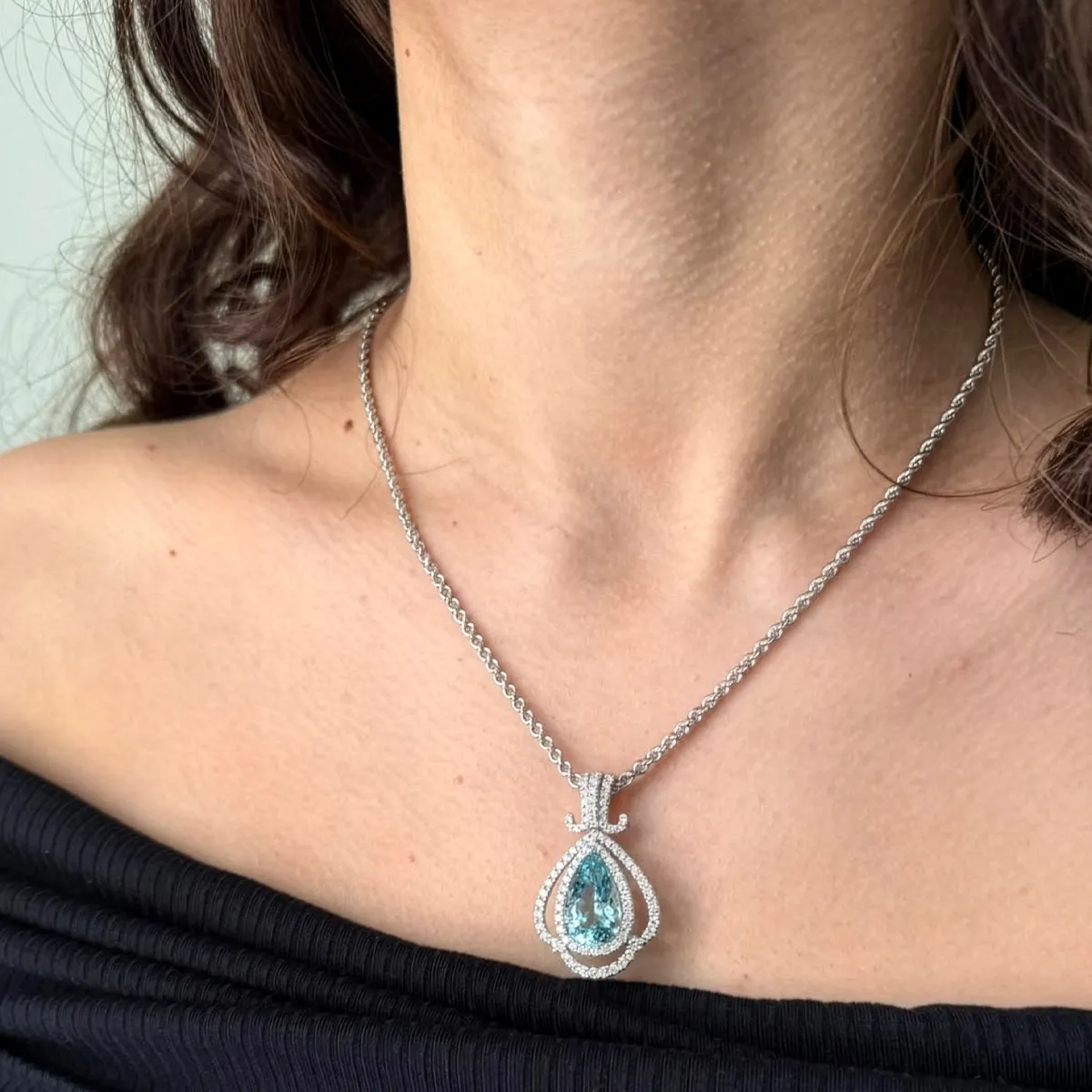Elegant silver necklace with a pear-shaped blue gemstone pendant, worn by a woman with a bare shoulder.