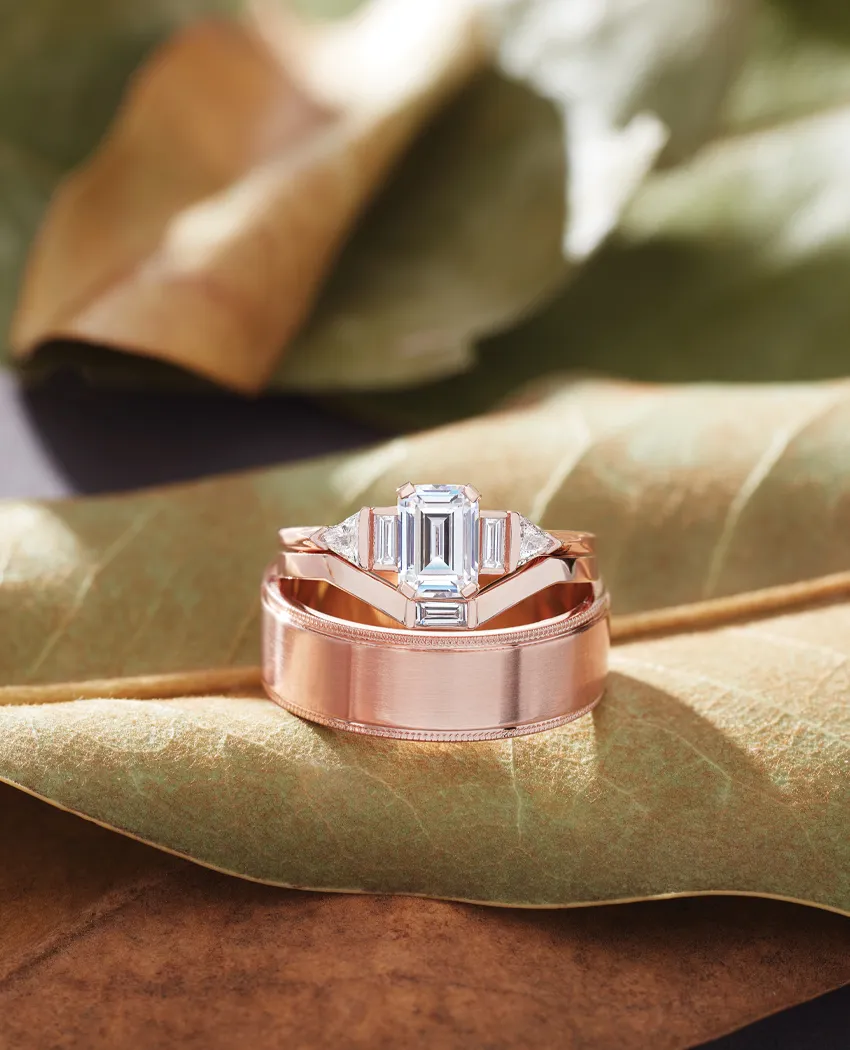 Elegant rose gold engagement ring set on leaves, featuring a central emerald-cut diamond.