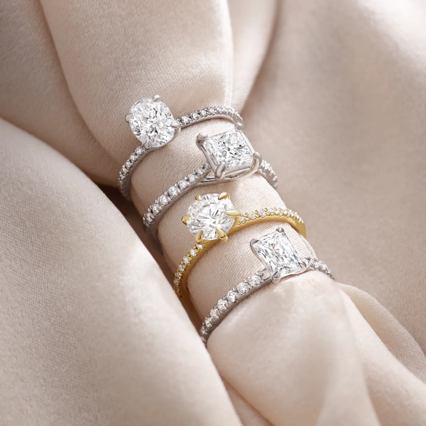 Four elegant diamond rings displayed on soft fabric, showcasing various styles and settings.