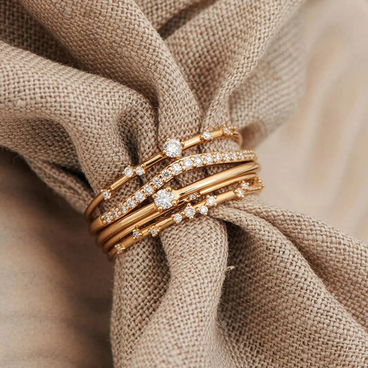 Elegant gold rings with diamonds arranged on a textured fabric background.