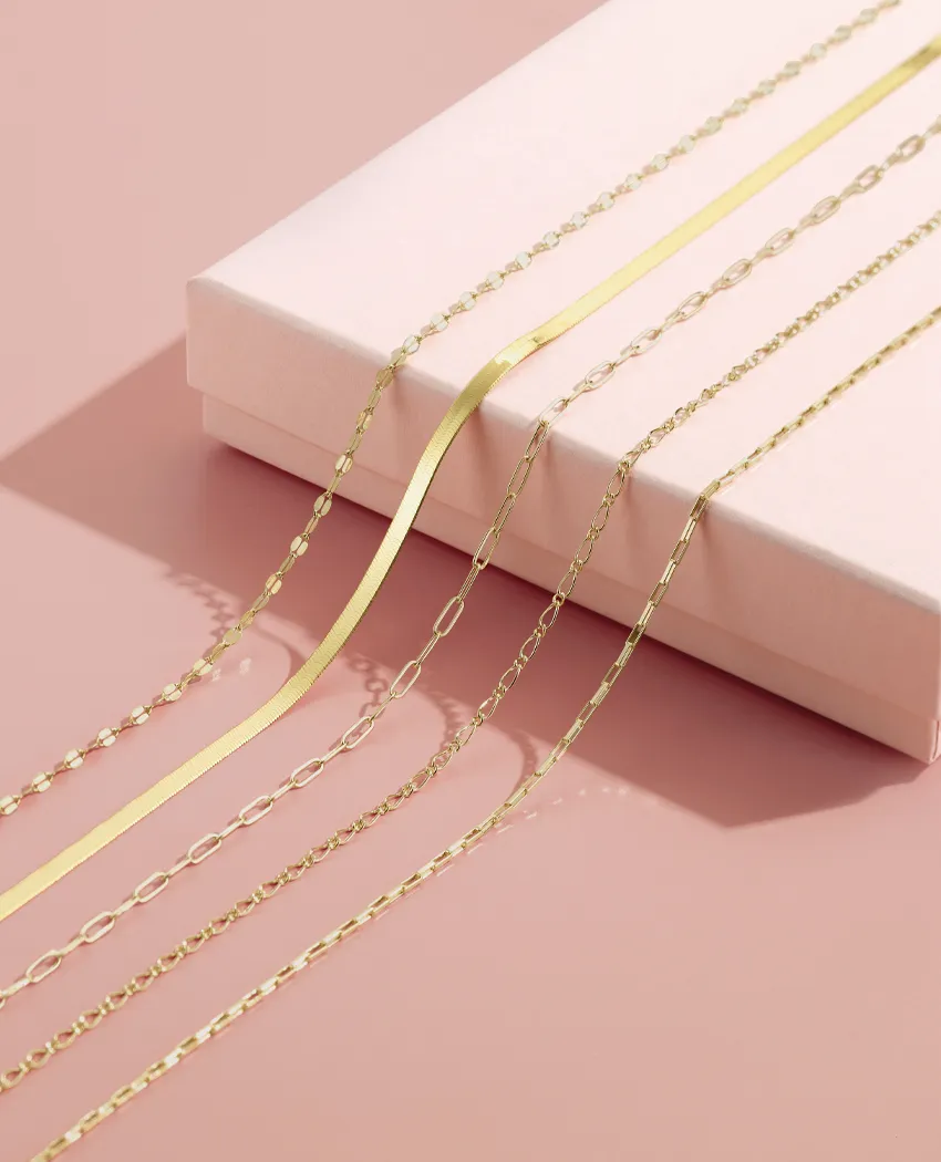 Gold chains displayed on a pink background, with a box underneath.