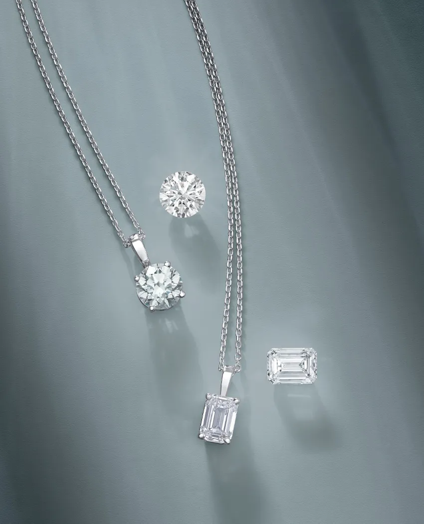 Two elegant diamond necklaces and two loose diamonds on a soft gray background.