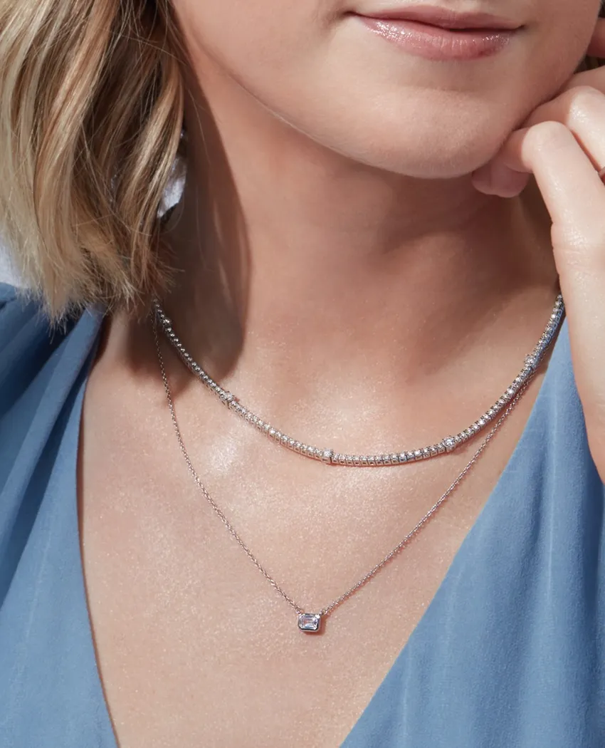 Model wearing layered silver necklaces with a sparkling pendant.