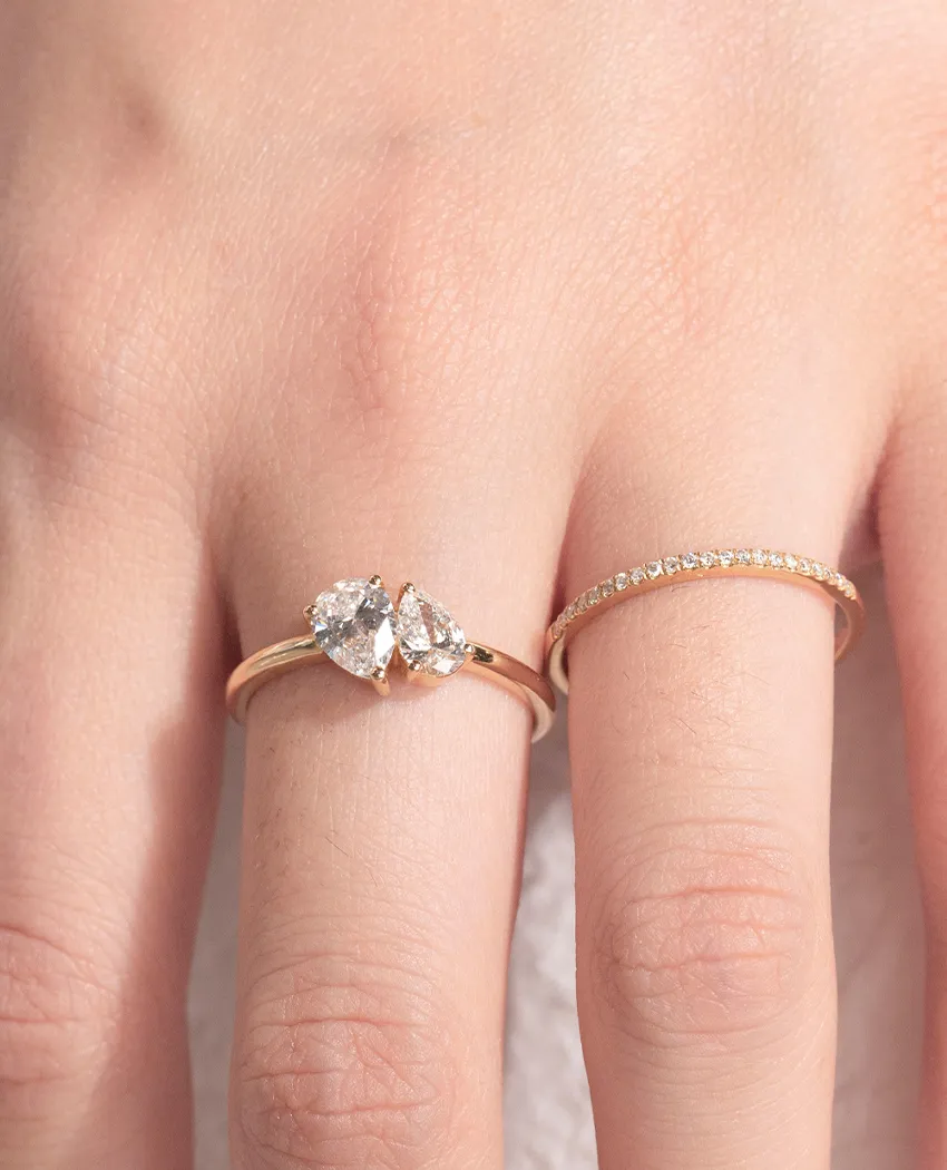 Two elegant rings on a hand: one with pear-shaped diamonds and the other a simple band. Click to Shop Rings at Golden Gifts Jewe